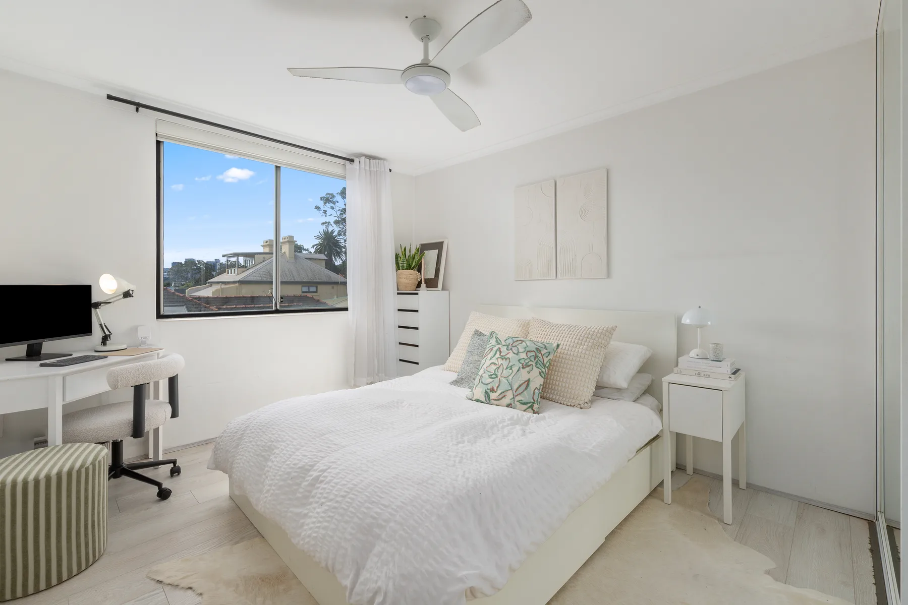 Un dormitorio luminoso con una cama y un escritorio junto a la ventana.