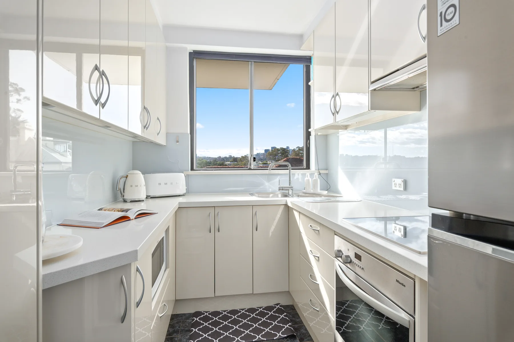 Una cocina luminosa con armarios blancos y una ventana con vistas al exterior.