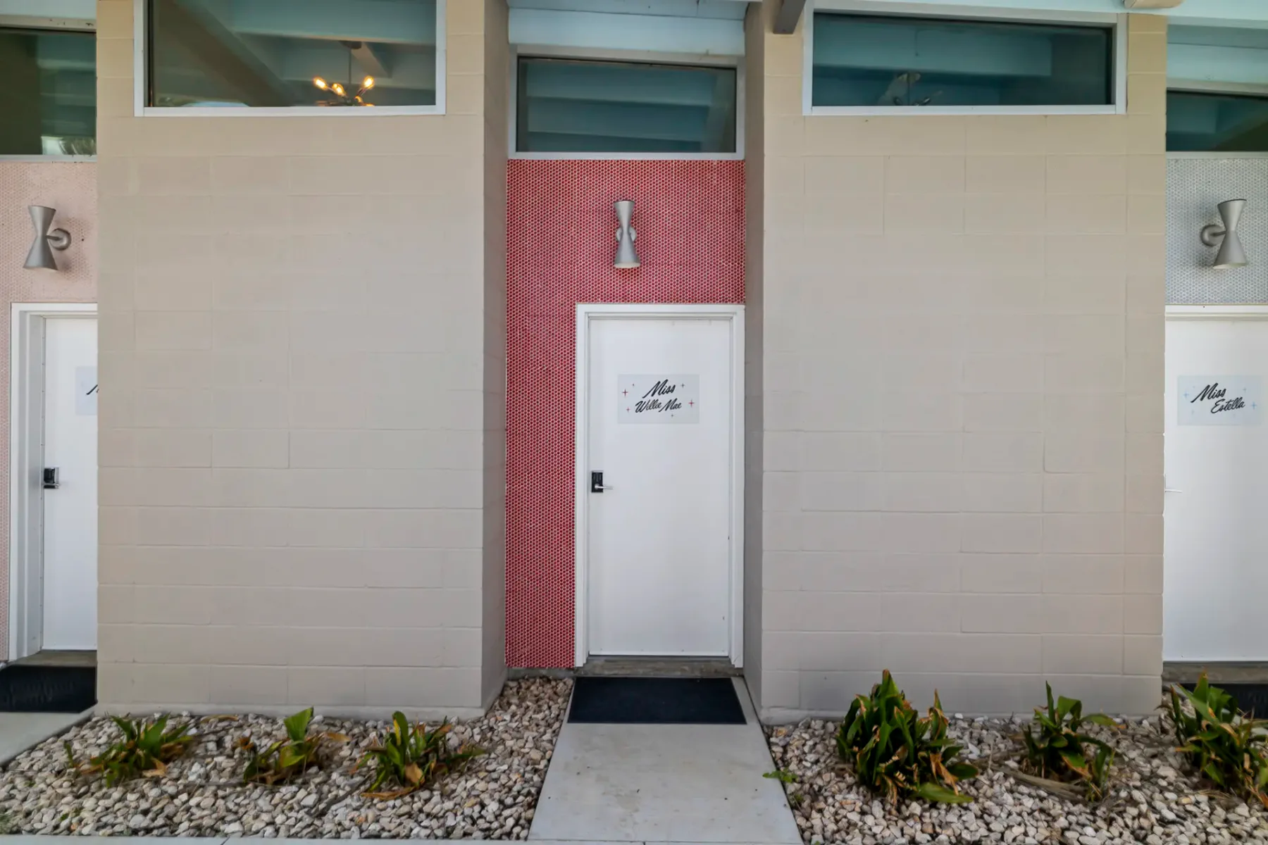 Zona de ducha exterior minimalista con suelo de hormigón, paredes beige y una pequeña jardinera con plantas verdes.