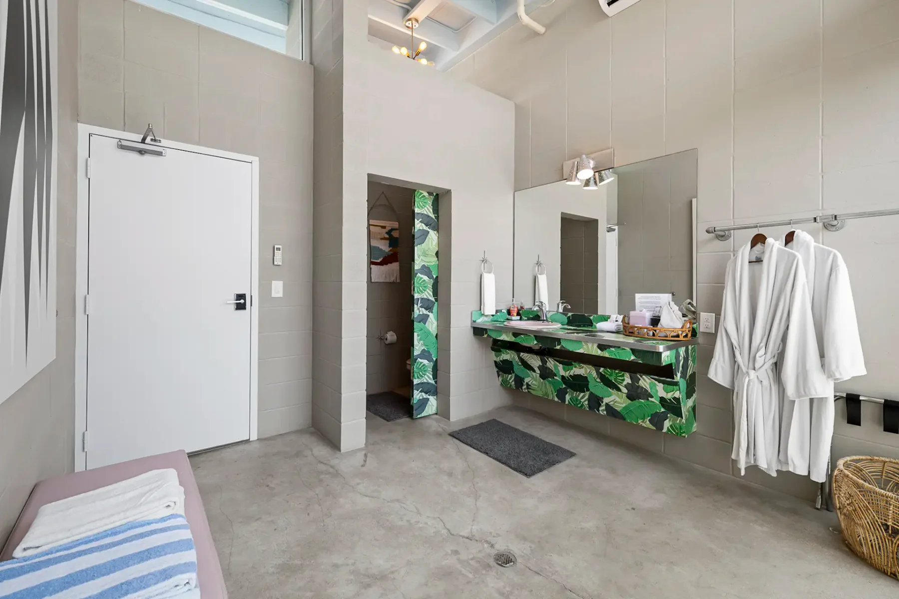 Baño moderno con lavabo de estampado tropical, albornoces en ganchos y una ventana grande. Decoración minimalista con arte abstracto y tonos neutros.
