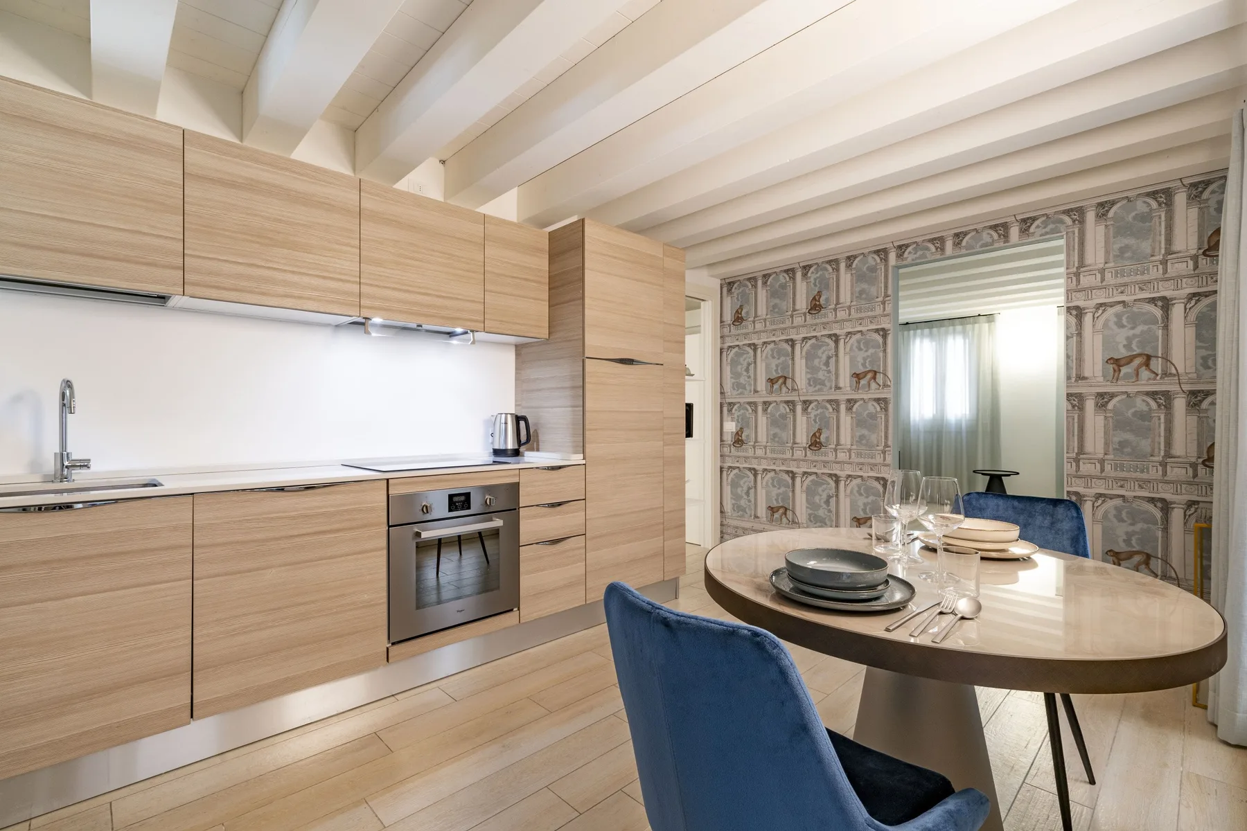 Una cocina moderna y zona de comedor con gabinetes de madera clara y una mesa redonda.