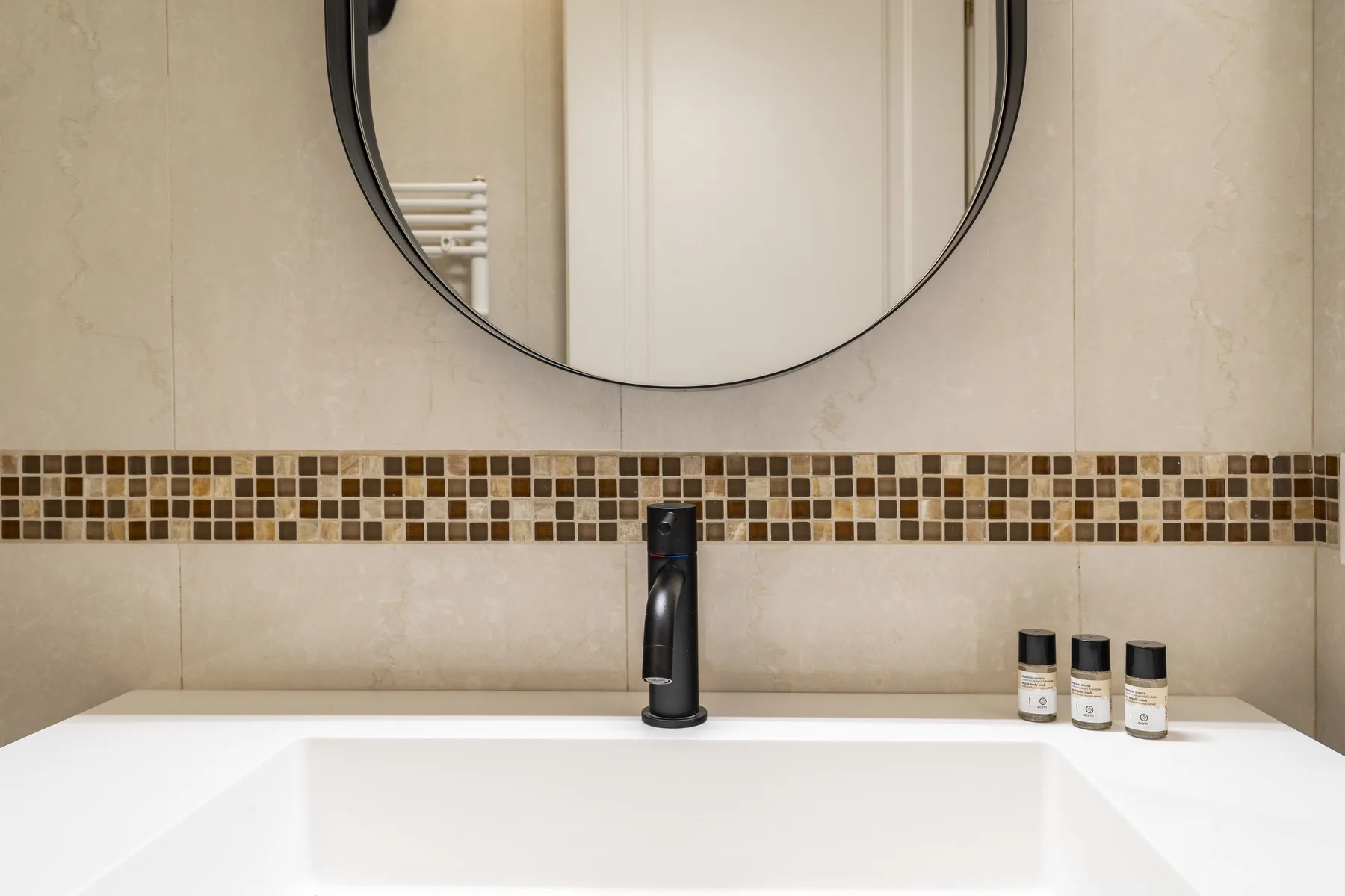 Un lavabo de baño con lavamanos blanco, grifo oscuro y espejo redondo.