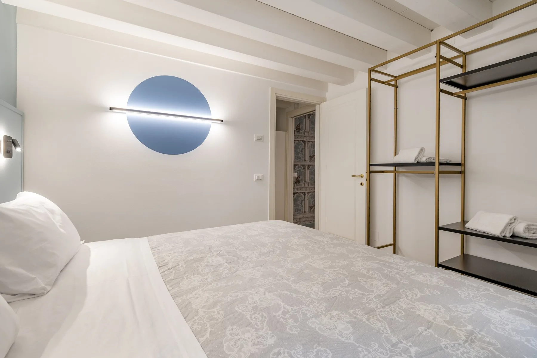 Un dormitorio con una cama bien arreglada y estantes abiertos junto a la pared.
