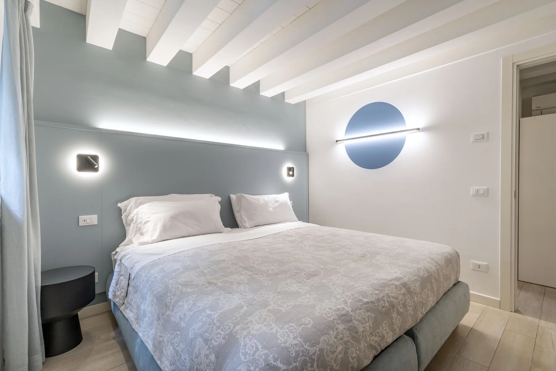 Un dormitorio con una cama grande, luces de pared y vigas vistas en el techo.
