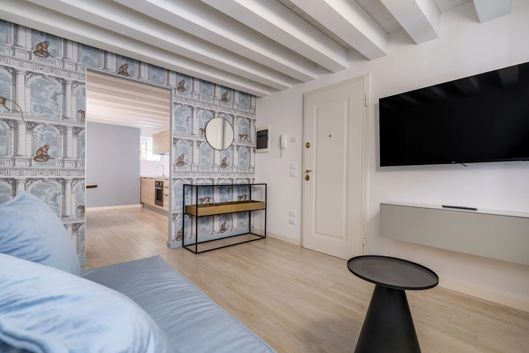 Una sala de estar con un sofá azul, papel tapiz estampado y un televisor en la pared.