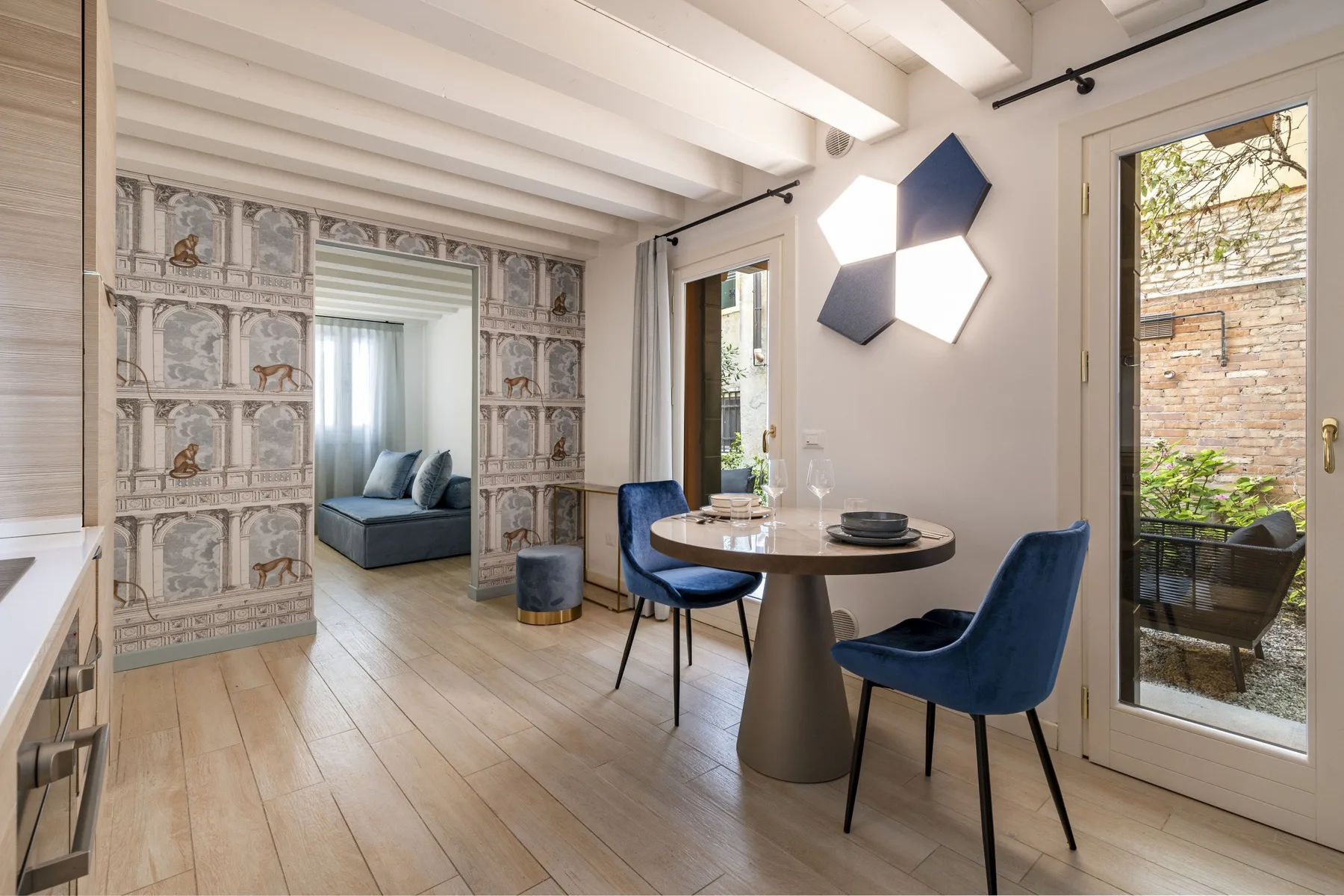 Un comedor luminoso con una mesa redonda, asientos azules y puertas que dan a un balcón.