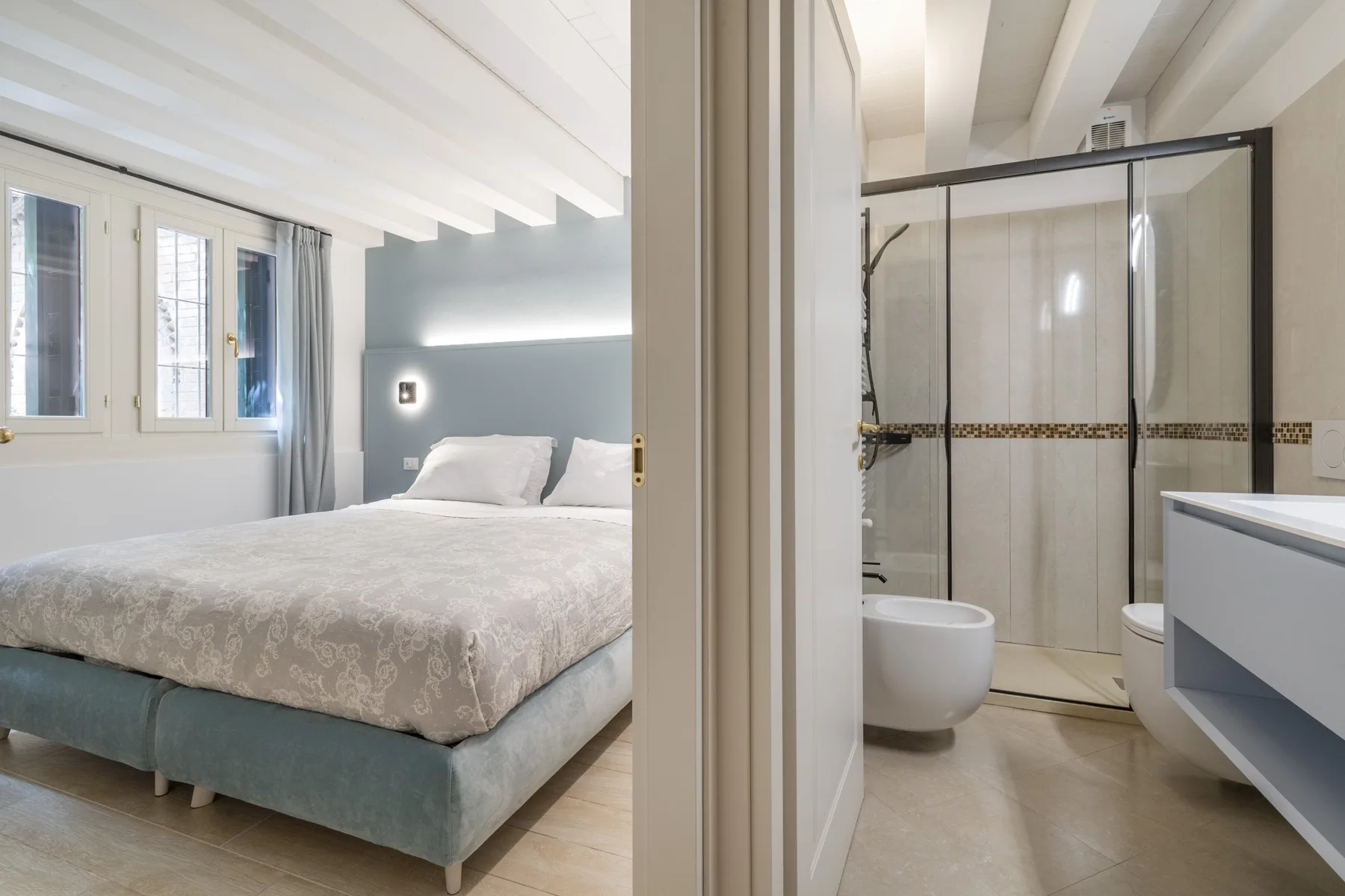 Se ve un dormitorio con una cama grande junto a un baño con ducha de vidrio.