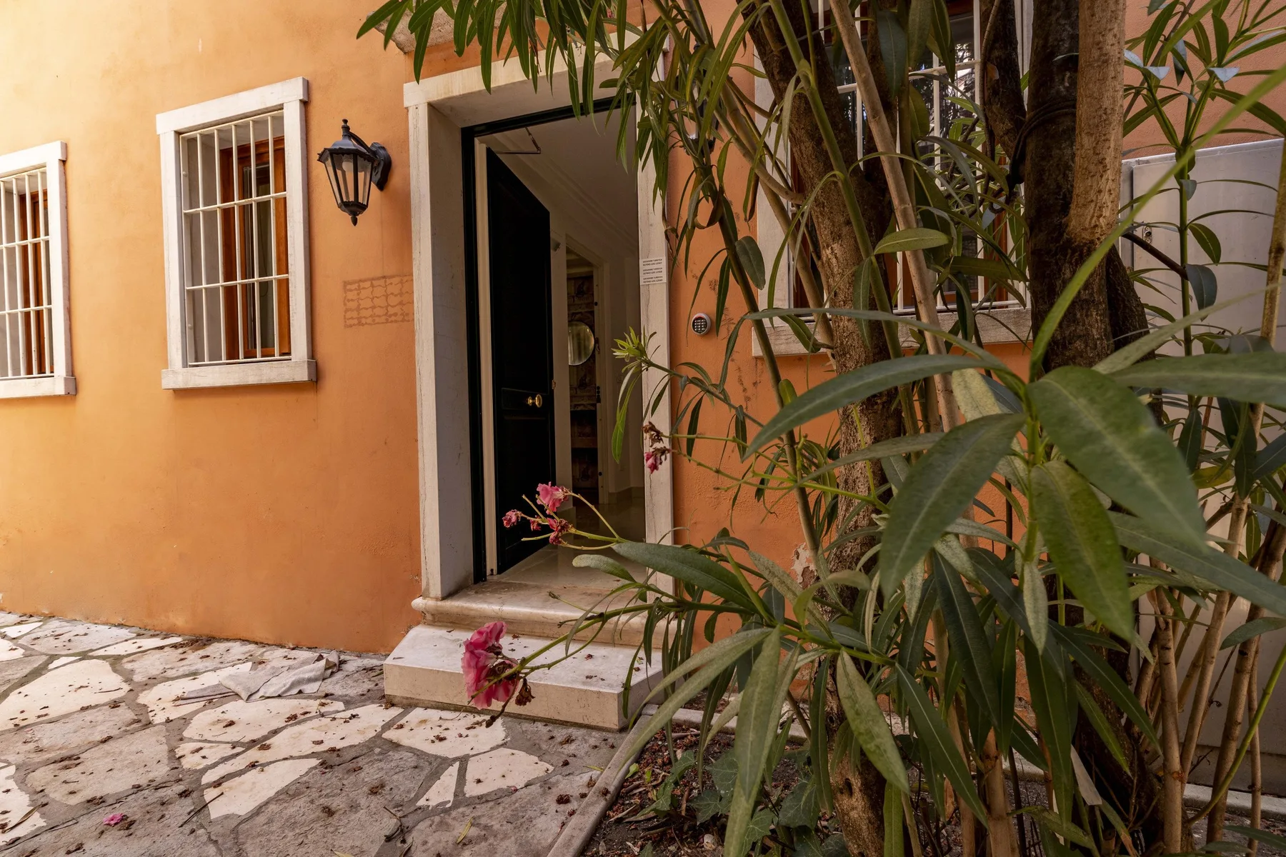 Una entrada exterior con una puerta abierta, ventanas y plantas frondosas.