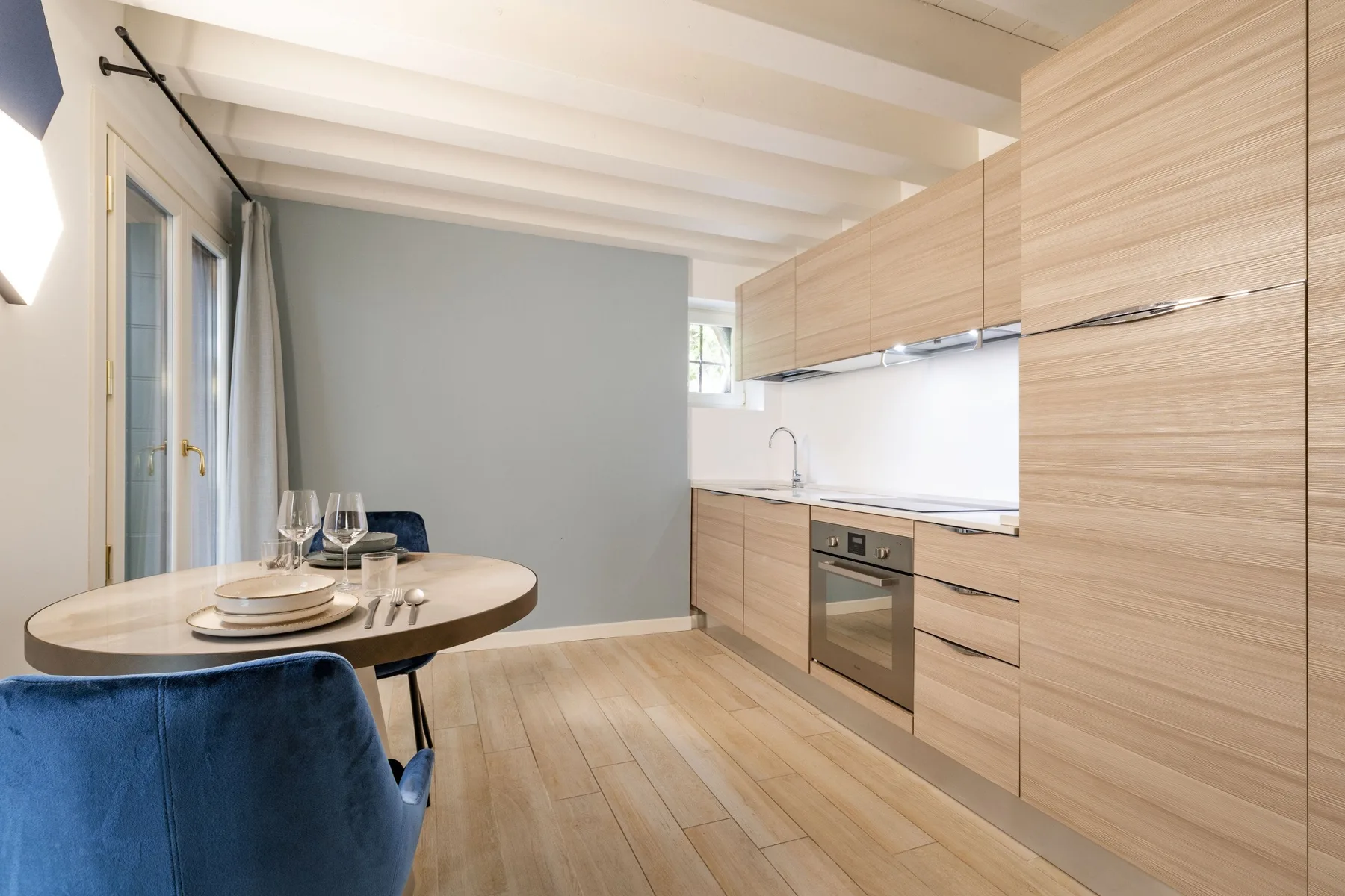 Una cocina y zona de comedor modernas, con gabinetes de madera clara y una mesa redonda.