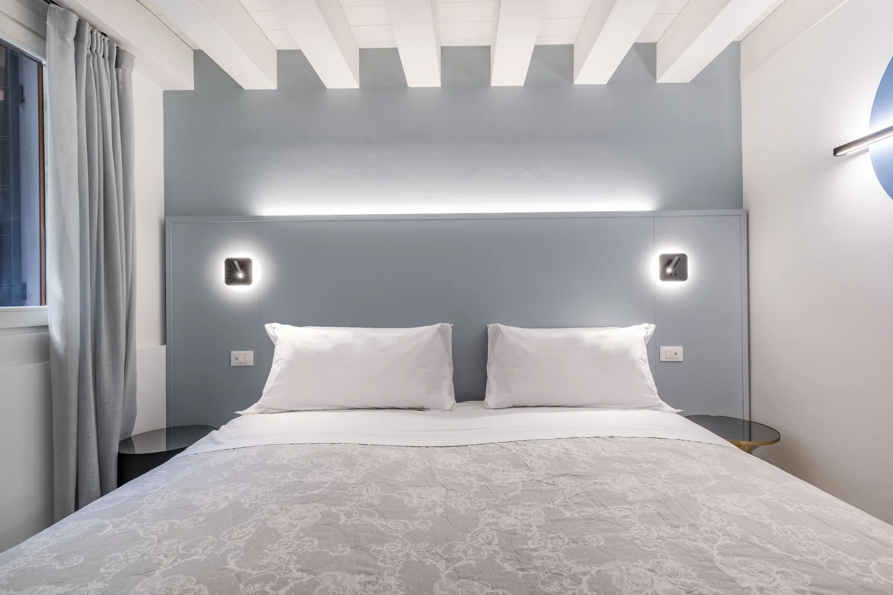 Un dormitorio con una cama bien hecha frente a una pared gris.