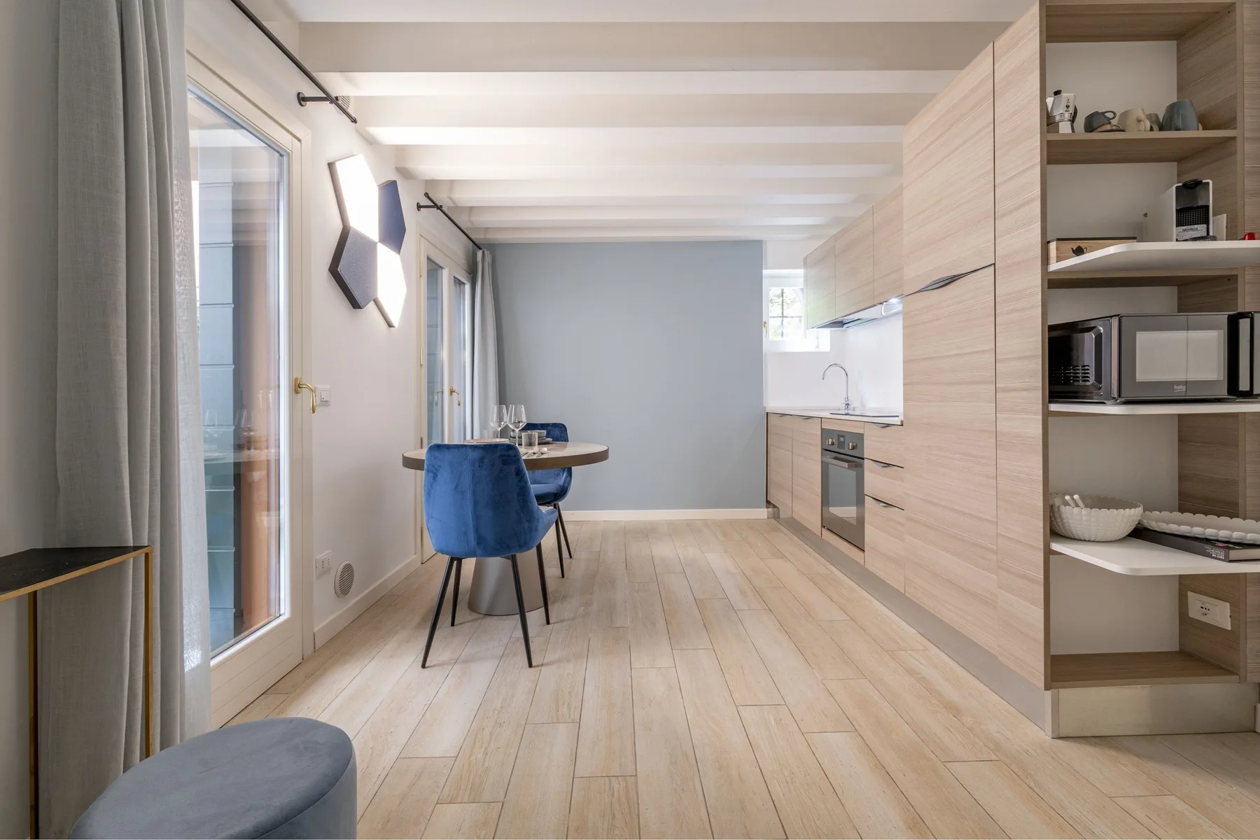 Una luminosa zona abierta de comedor y cocina, con asientos azules y armarios de madera clara.