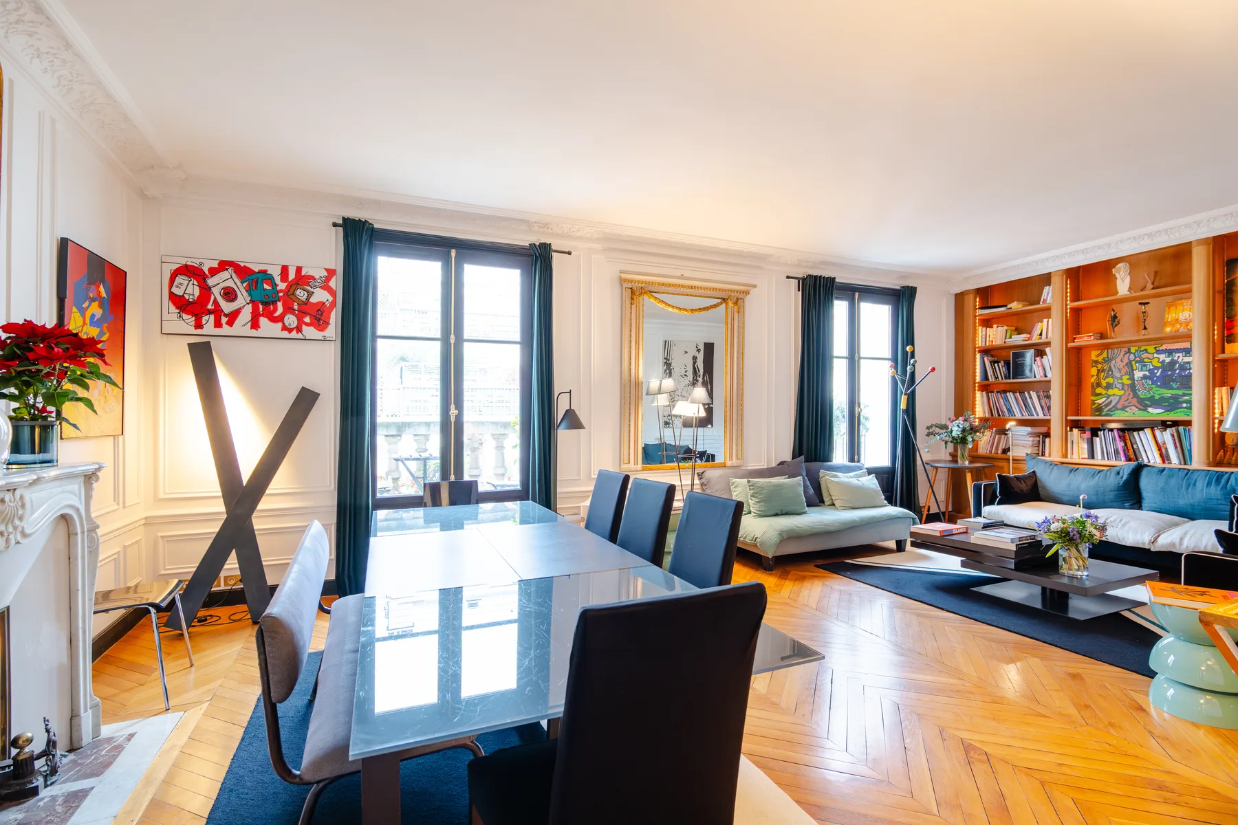 A bright living and dining room has a glass table, seating, and bookshelves.
