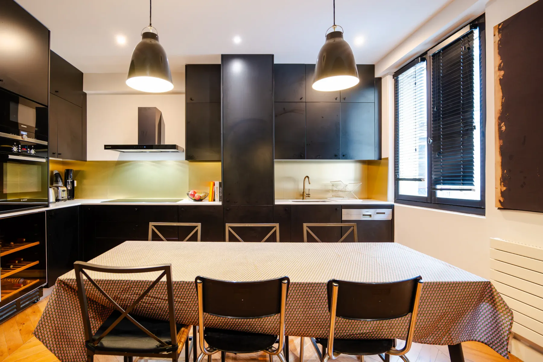 A dining table and chairs sit in a modern kitchen with dark cabinets.