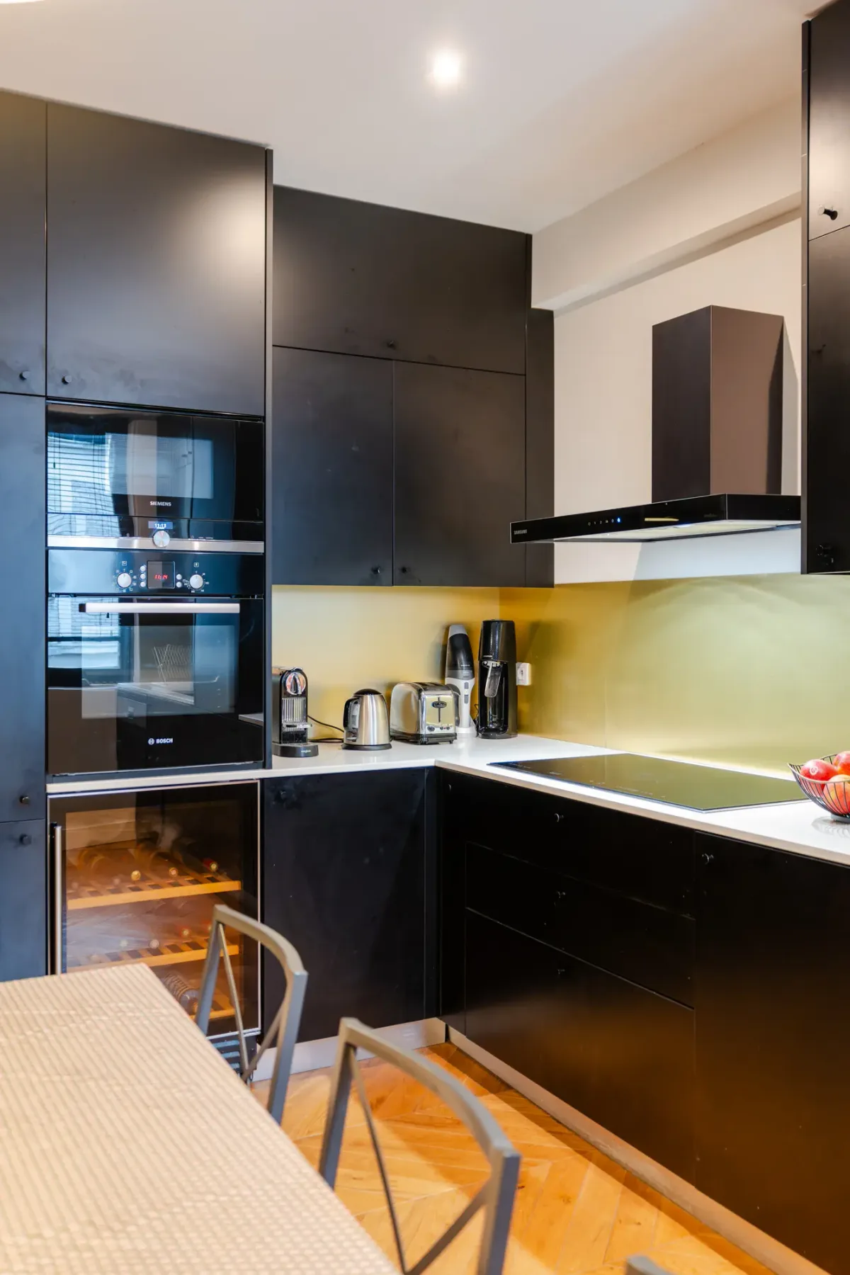 A modern kitchen with dark cabinets, built-in appliances, and a dining table.