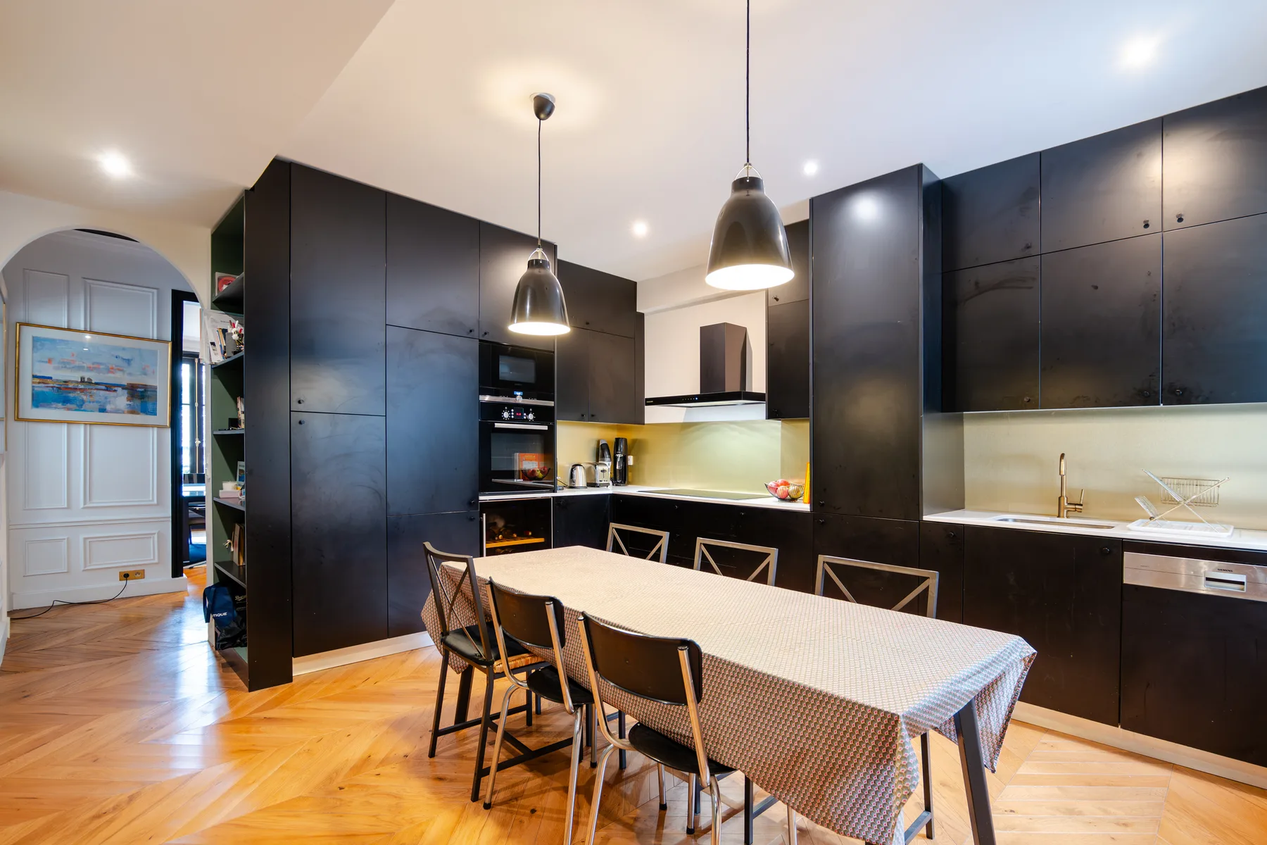 A modern kitchen and dining area with dark cabinetry and a long table.