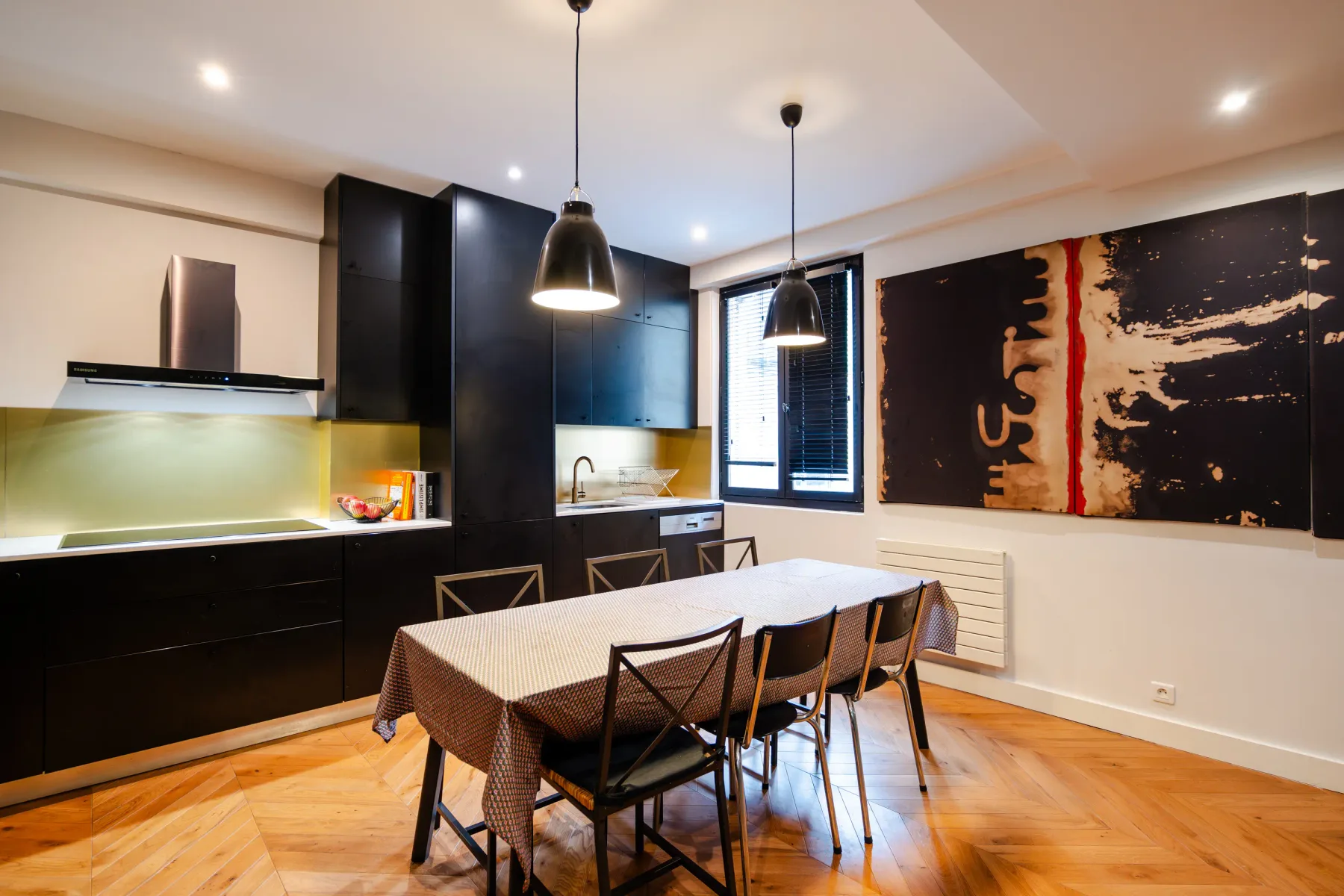 A dining area with a long table beside a dark kitchen.