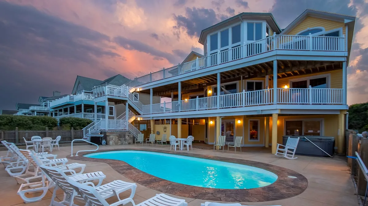 Una amplia piscina exterior está junto a una casa de varios niveles al atardecer.