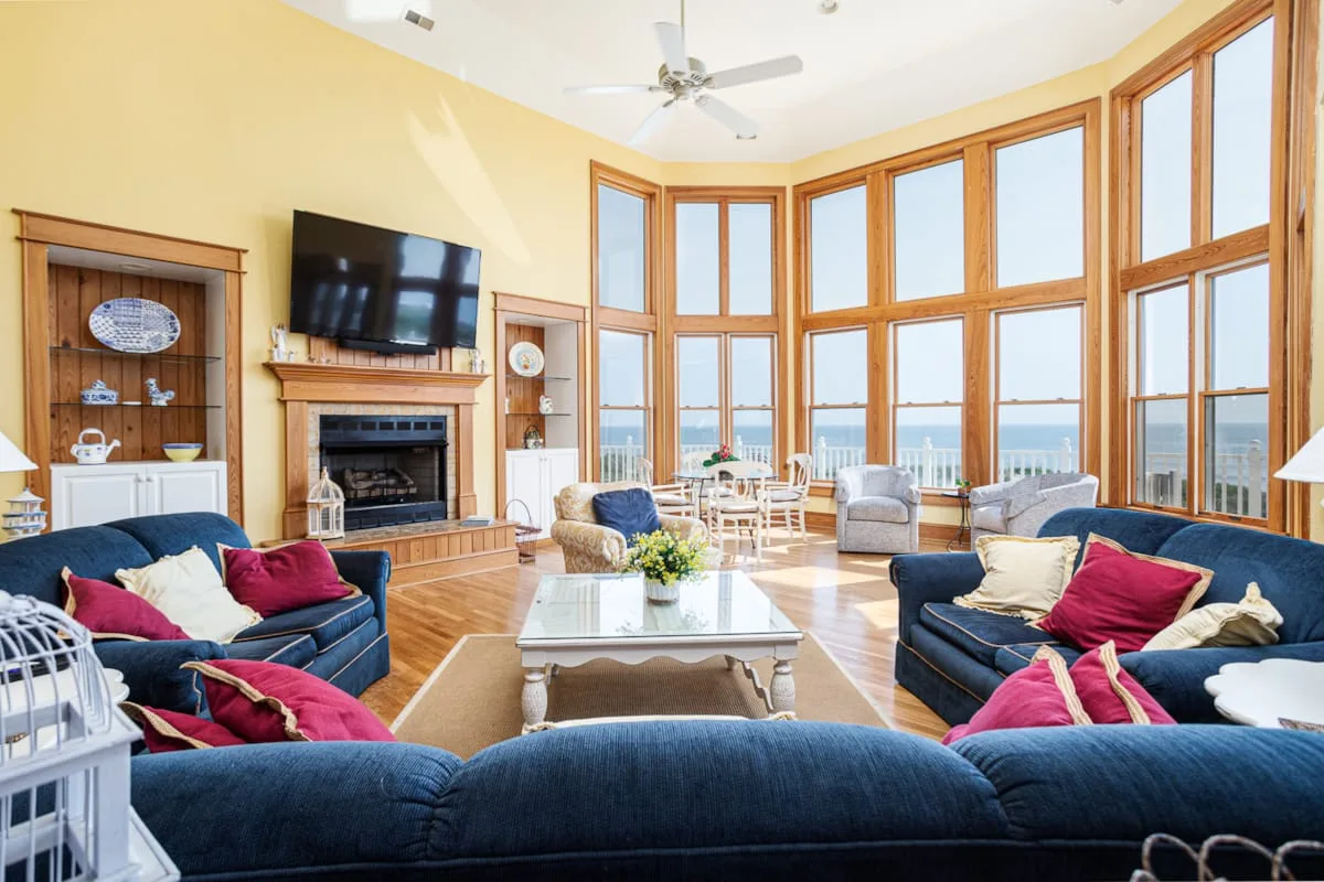 Una sala de estar luminosa con asientos, chimenea y grandes ventanas con vistas al agua.