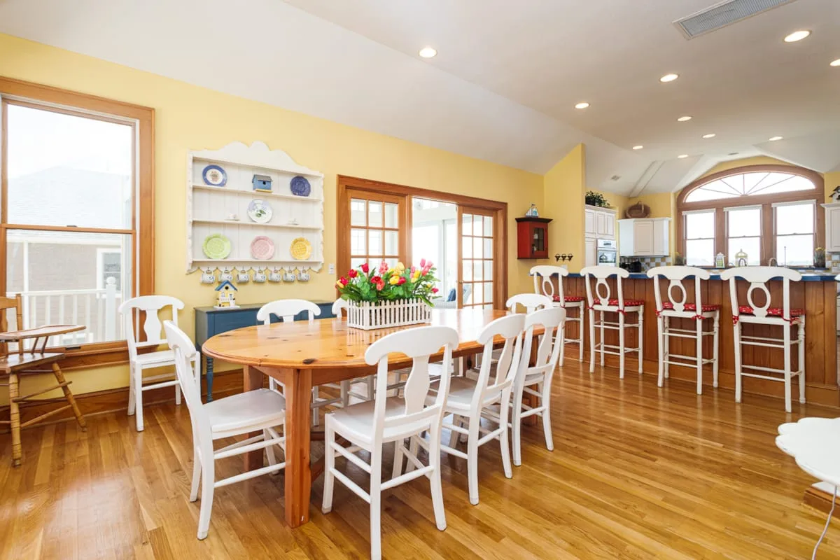 Un comedor luminoso con una mesa de madera y asientos blancos junto a una cocina abierta.