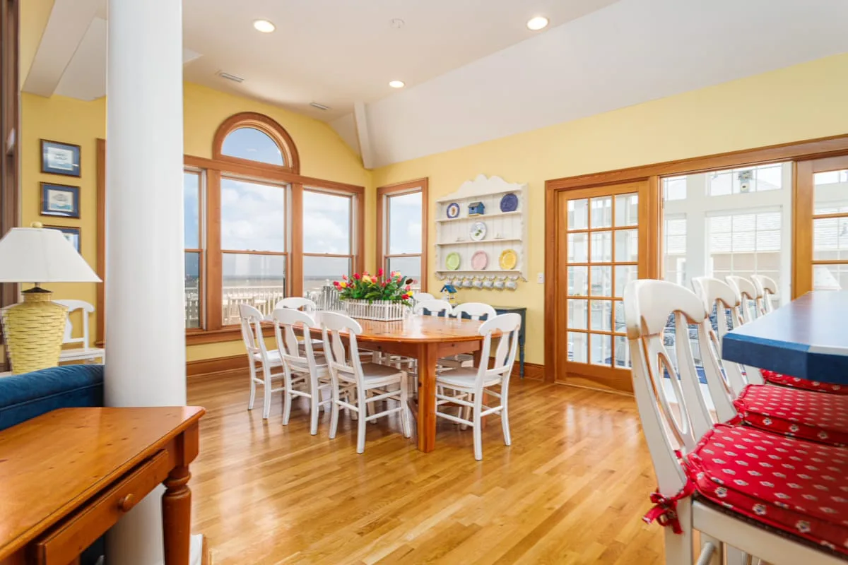 Un comedor luminoso con una mesa larga y sillas junto a grandes ventanas.
