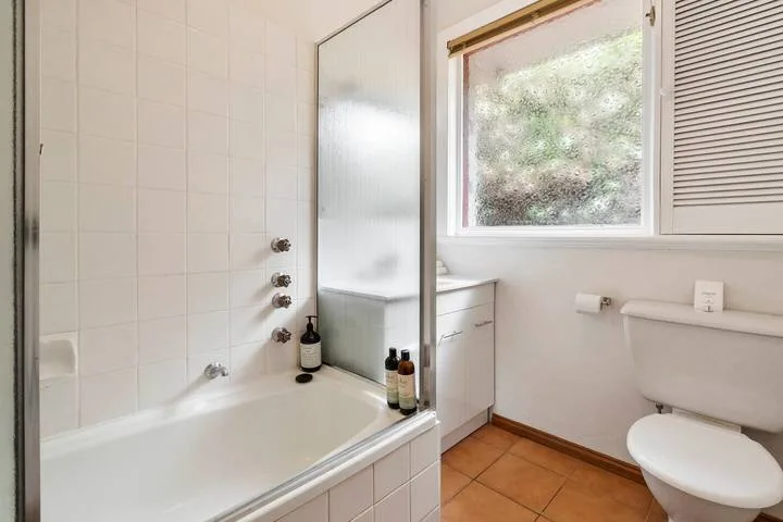 Un baño alicatado con bañera, ventana e inodoro.