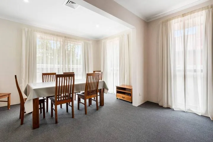 Un comedor luminoso con una mesa de madera y sillas junto a grandes ventanas con cortinas.