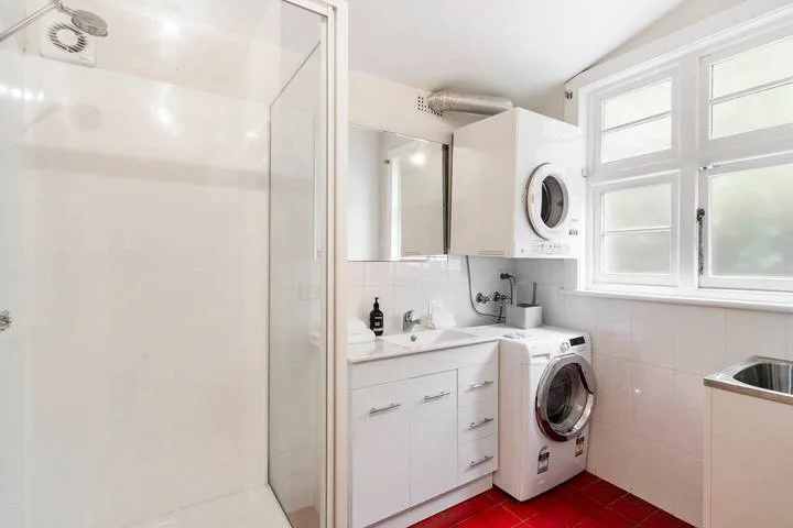 Un baño luminoso con ducha, lavabo y lavadora.