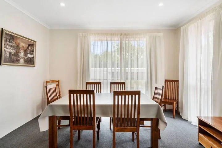 Un comedor con una mesa y sillas de madera junto a grandes ventanas con cortinas.