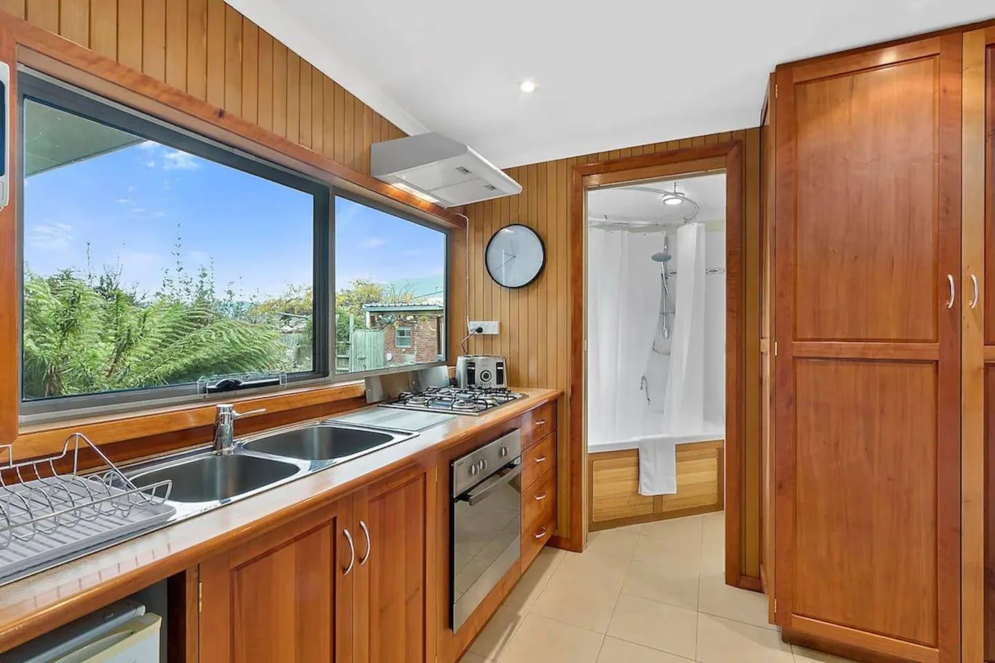 Una cocina con fregadero, placa de cocción y una gran ventana con vistas a la vegetación.