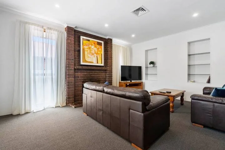 Una sala luminosa con asientos oscuros, un televisor y ventanas altas con cortinas.