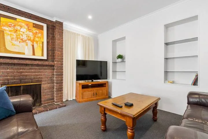 Sala de estar con televisor, mesa de centro de madera y pared de ladrillo.