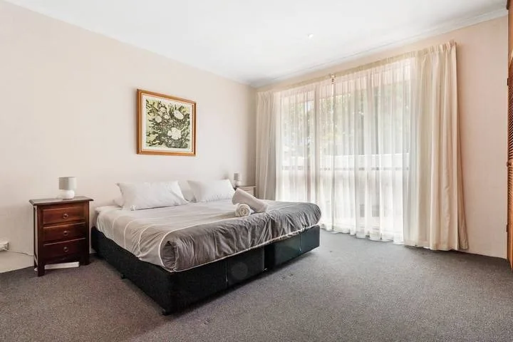 Un dormitorio con una cama, una mesita de noche y cortinas sobre una ventana grande.