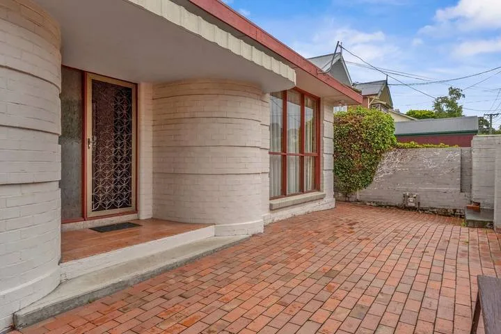 Un patio pavimentado con ladrillos junto a un edificio con ventana y entrada.