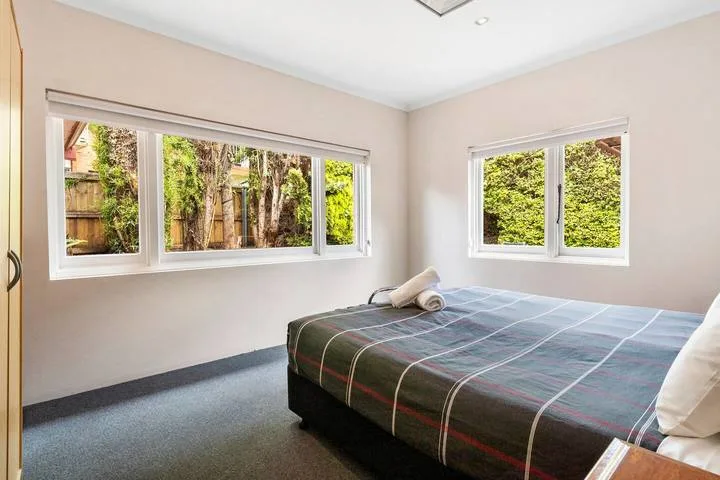 Un dormitorio con una cama bajo dos ventanas con vistas a la vegetación.