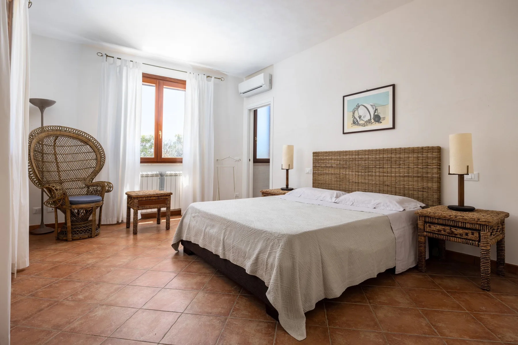 A bedroom with a large bed, woven headboard, and a window with sheer curtains.