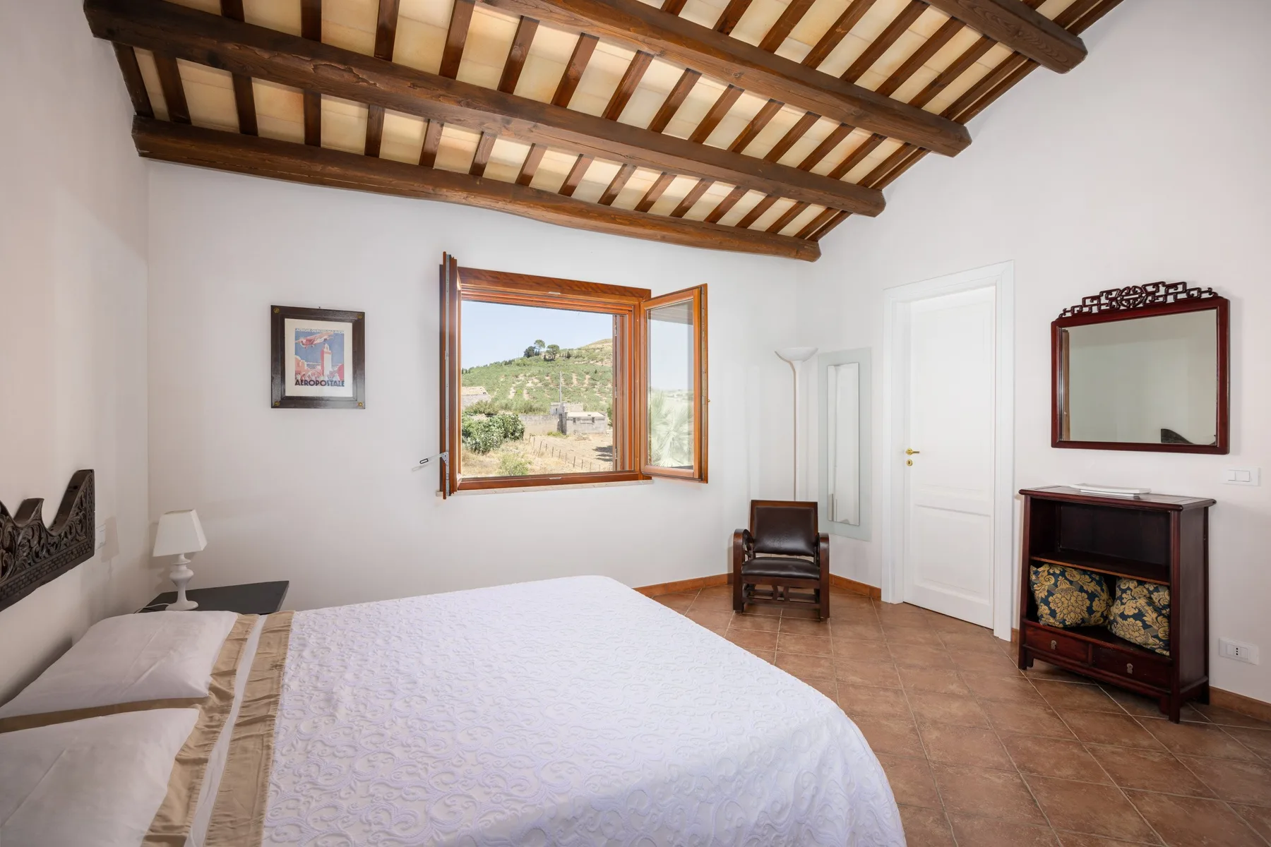 A bedroom with a bed, exposed wooden ceiling beams, and an open window.