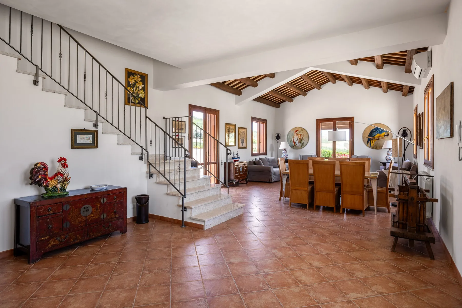 A spacious living and dining room with a staircase and wooden ceiling beams.