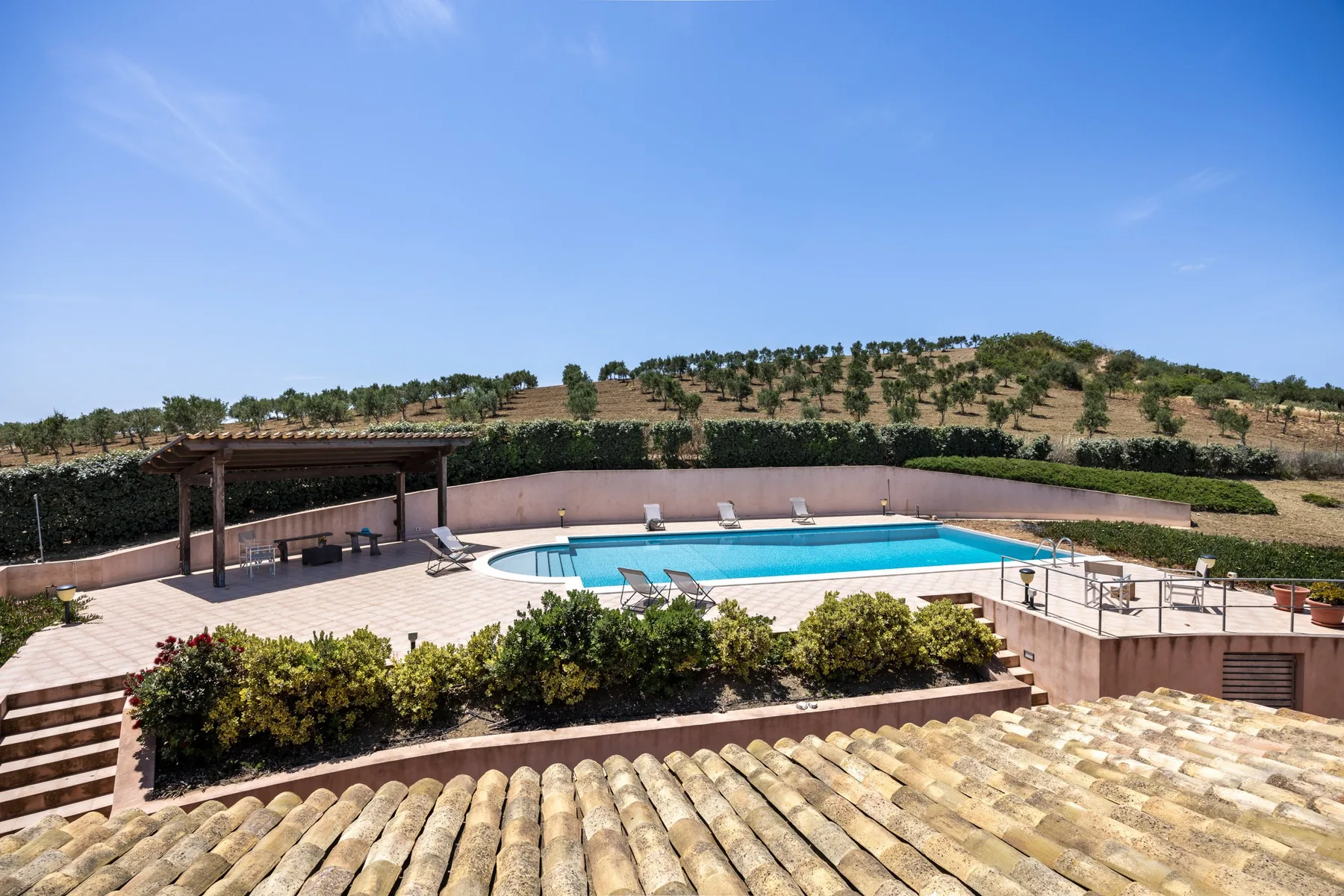 Outdoor swimming pool and paved patio overlook a dry, tree-covered hillside.
