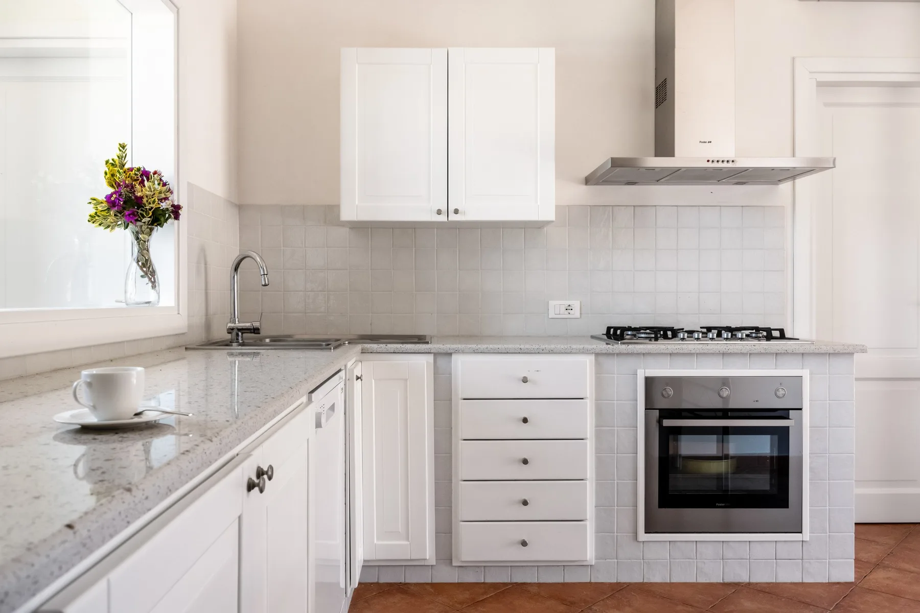 A bright kitchen with white cabinets, a countertop, and a built-in oven.
