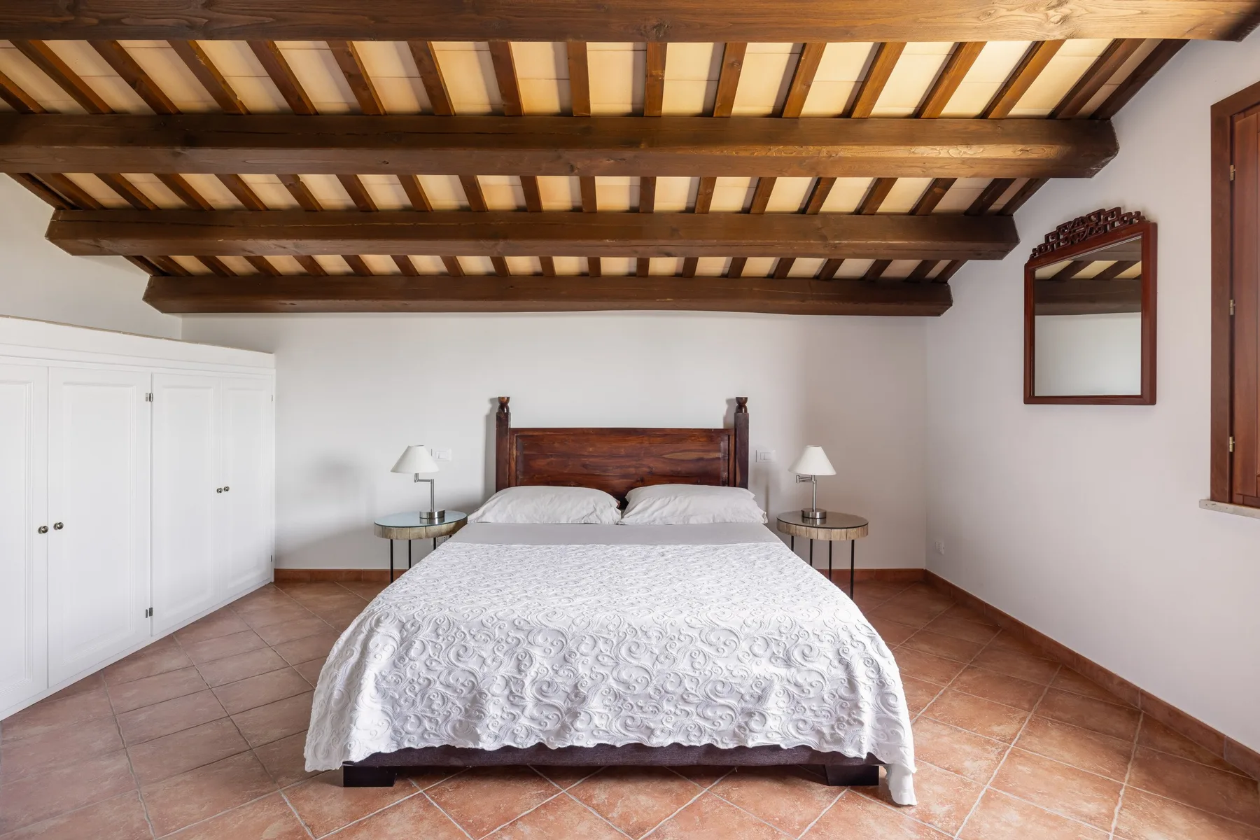 A bedroom with a bed beneath exposed wooden ceiling beams.