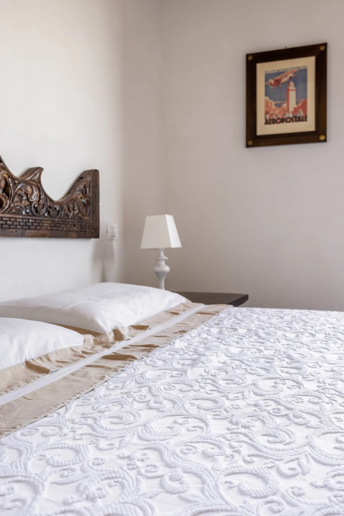 A bedroom with a patterned bedspread, carved headboard, and bedside lamp.