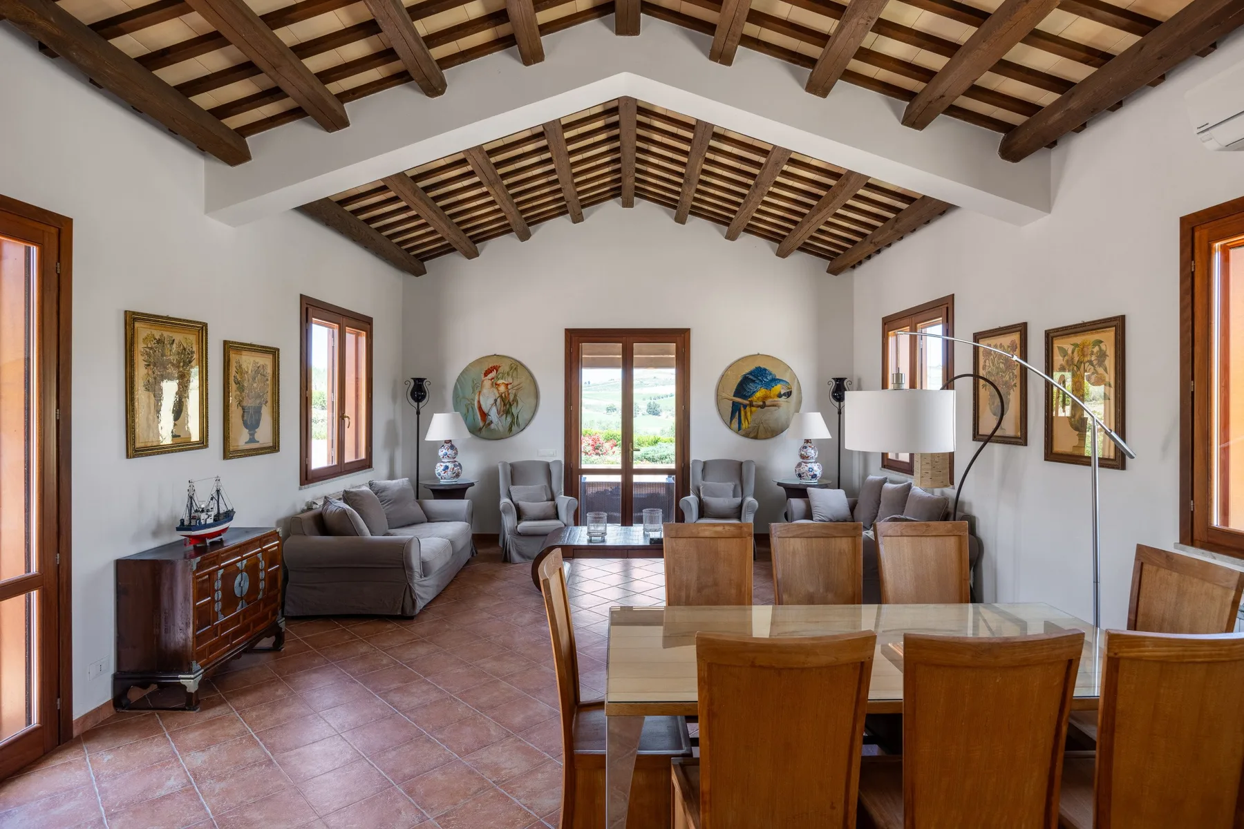 A dining and living room with a wooden table and seating beneath exposed beams.