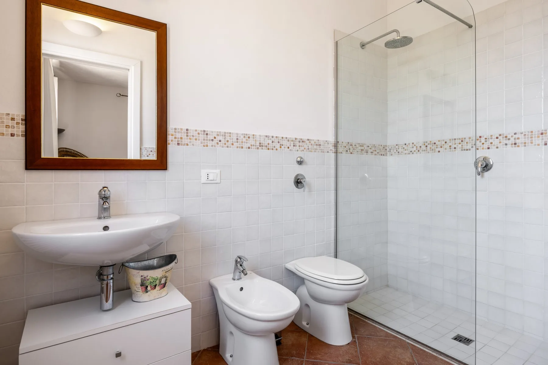 A tiled bathroom with a sink, toilet, bidet, and glass shower.