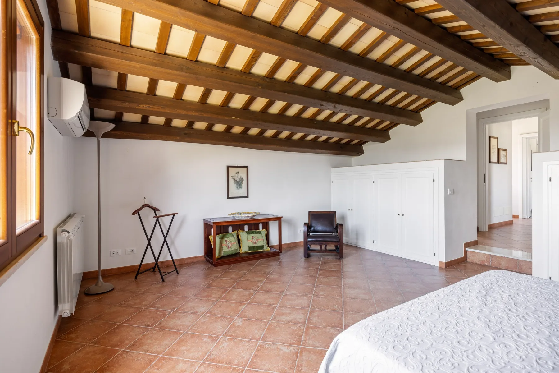 A spacious bedroom with exposed wooden ceiling beams and a bed in the foreground.