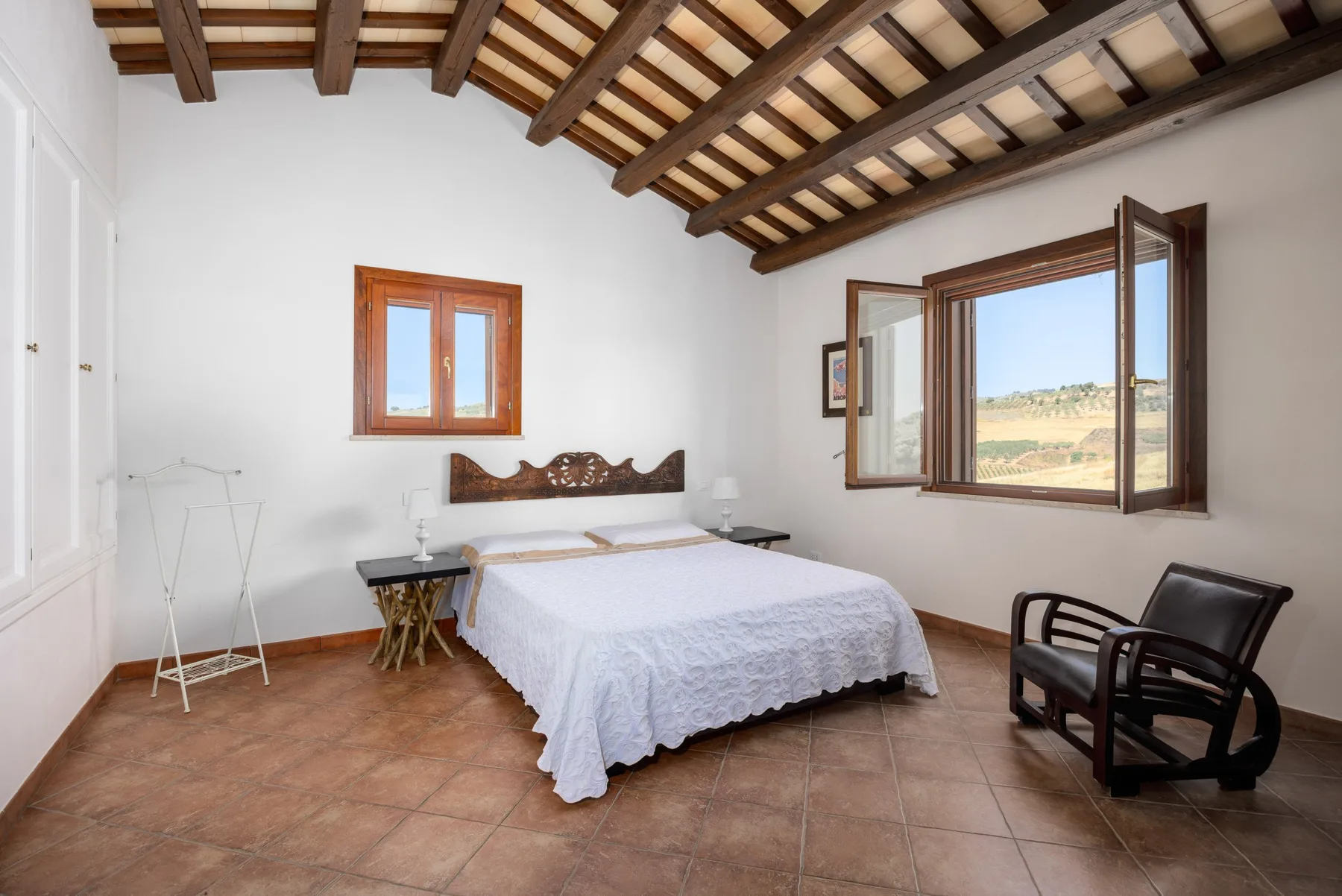 A bright bedroom with a bed, exposed ceiling beams, and an open window.