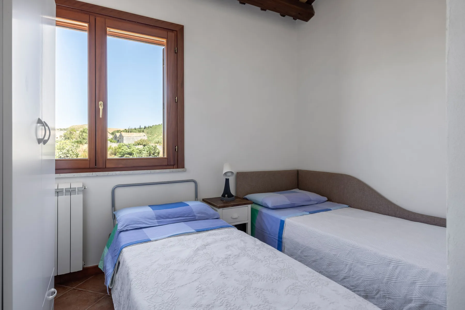 A bedroom with two beds and a window overlooking greenery.
