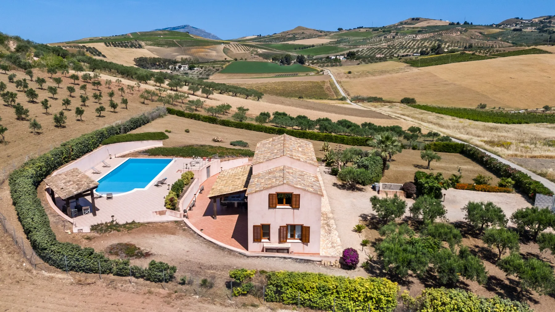 A countryside house with a swimming pool sits among rolling agricultural fields.