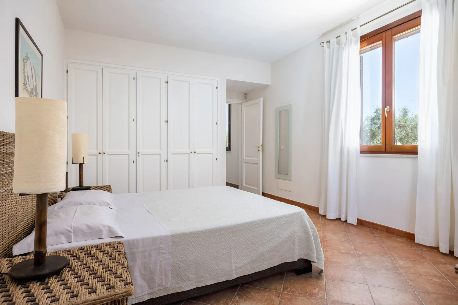 A bright bedroom with a bed, built-in wardrobes, and a window with curtains.