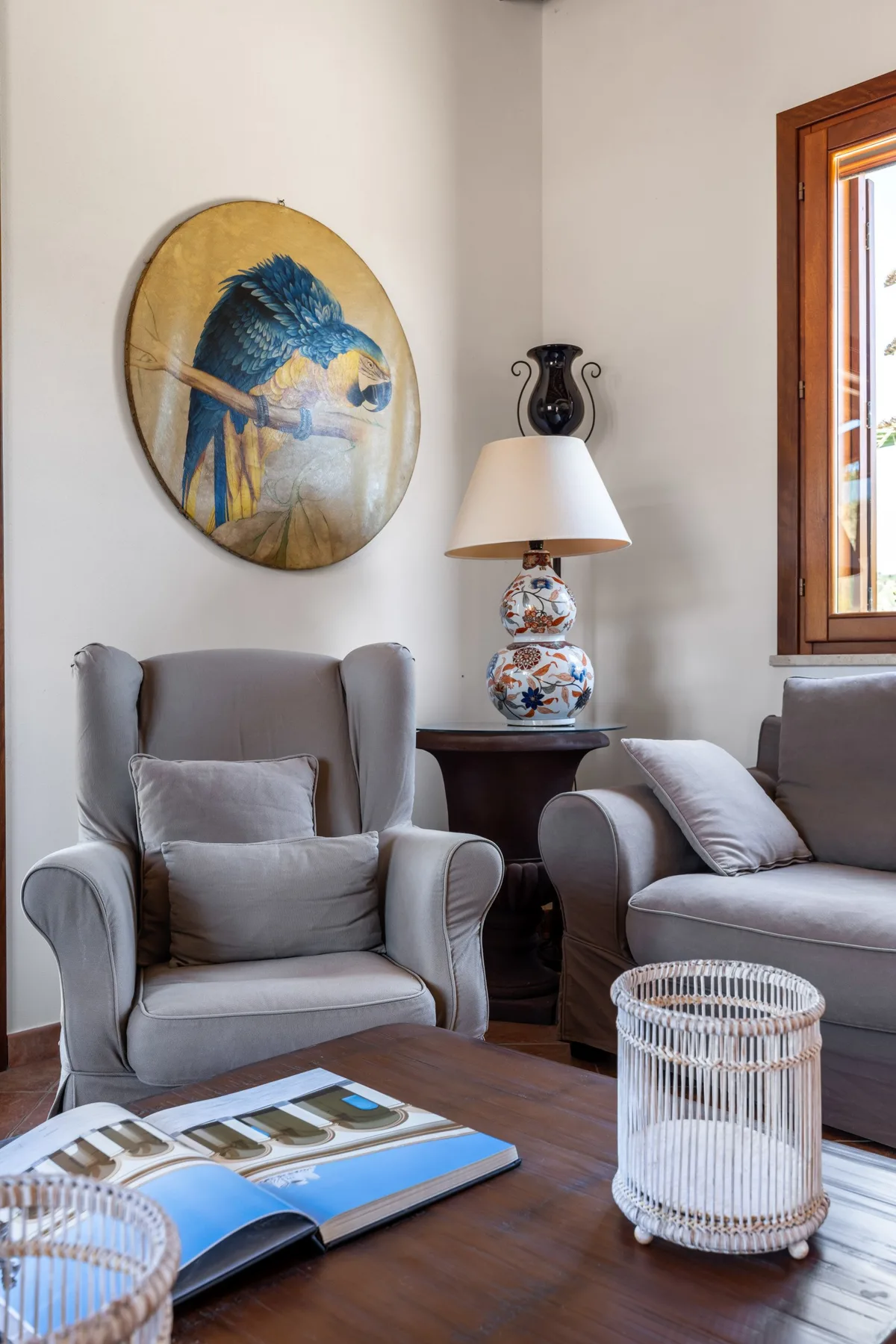 A living room seating area with gray armchairs and a round bird painting.