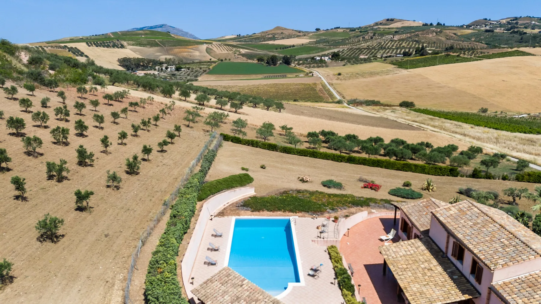 Aerial view of a swimming pool beside a building, surrounded by rolling farmland.